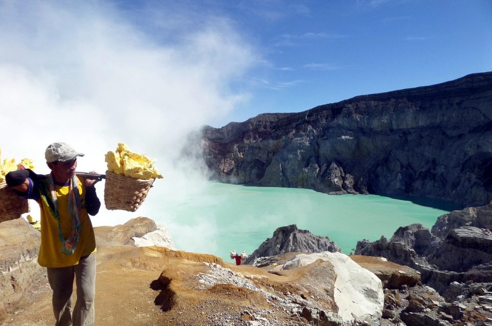 Turquoise acidic lake at Ijen Crater with local miners working along the crater rim.